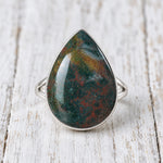 Silver bloodstone teardrop ring with a polished green and red stone on whitewashed wood