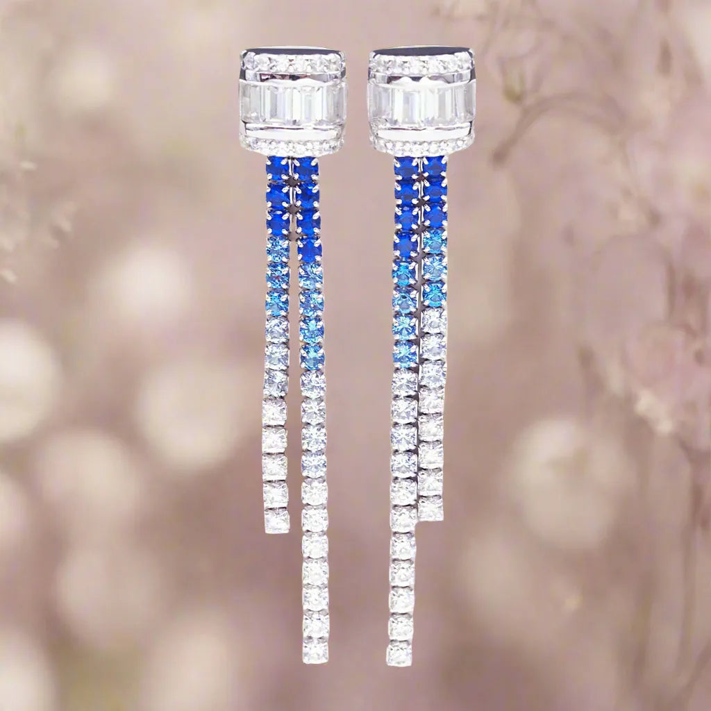 Pair of long, dangling earrings with blue and clear gemstones on a blurred background