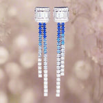 Pair of long, dangling earrings with blue and clear gemstones on a blurred background