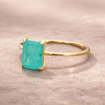 Gold ring with a green blue emerald cut natural tourmaline gemstone on a neutral background