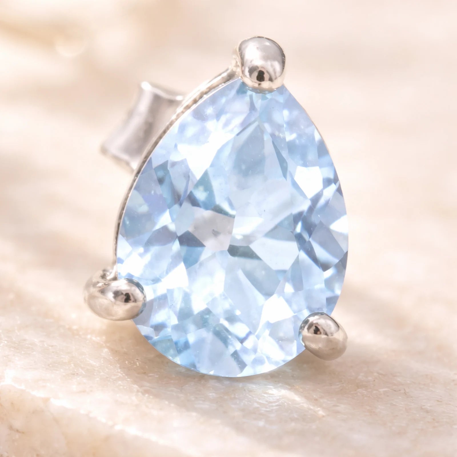 Sterling Silver Pear Shaped stud earring with faceted blue topaz gemstones on a light surface.