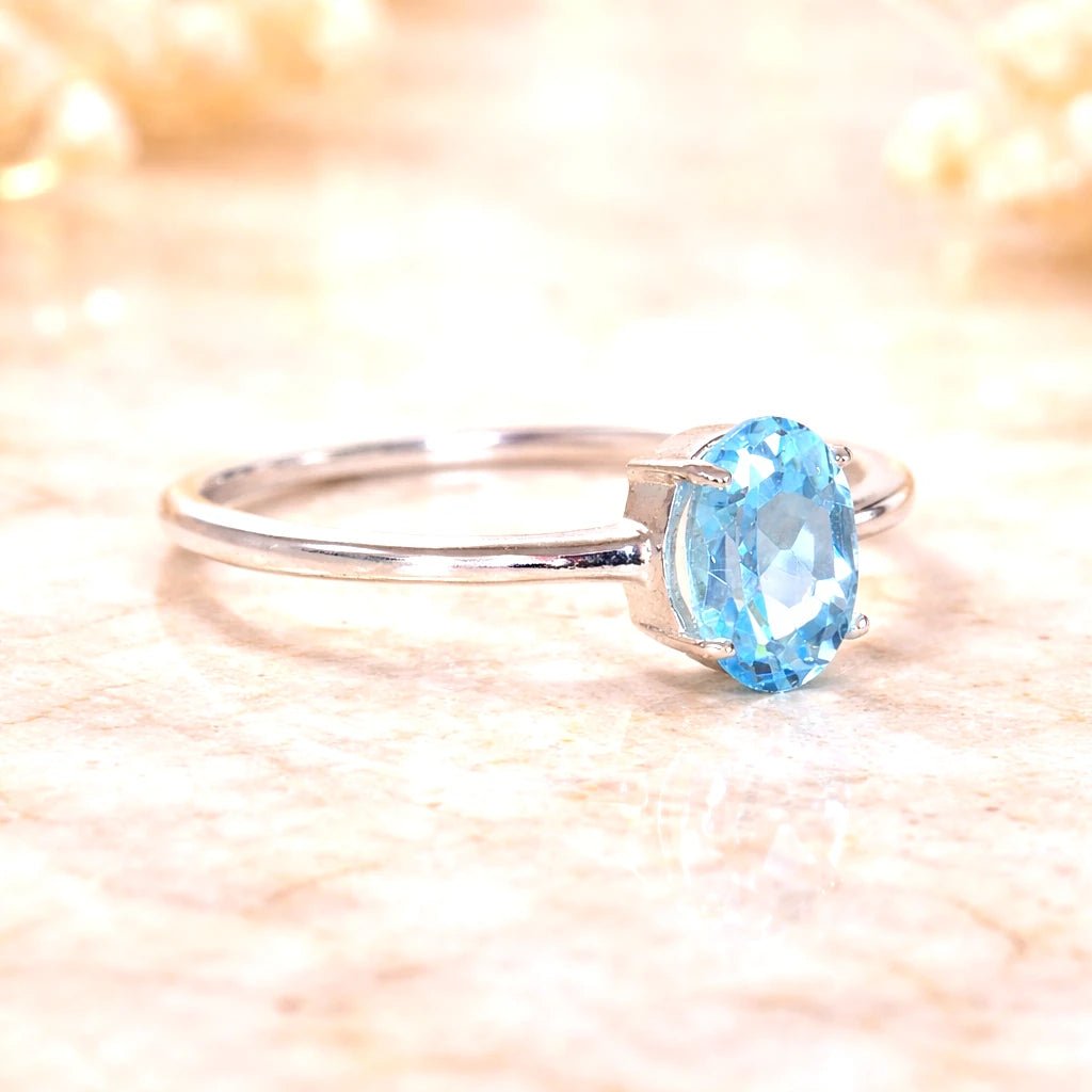 Sterling Silver ring with a oval faceted claw set natural blue topaz gemstone on a soft, blurred background