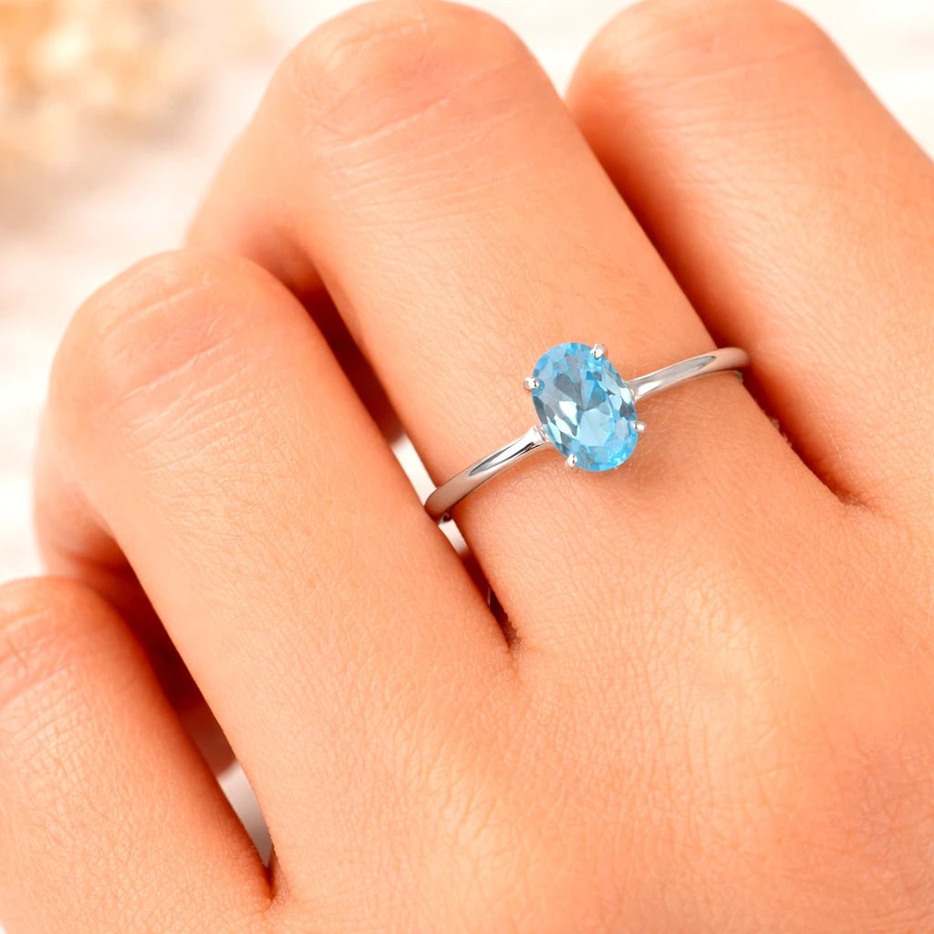 Silver ring with a blue topaz gemstone on a hand against a blurred background