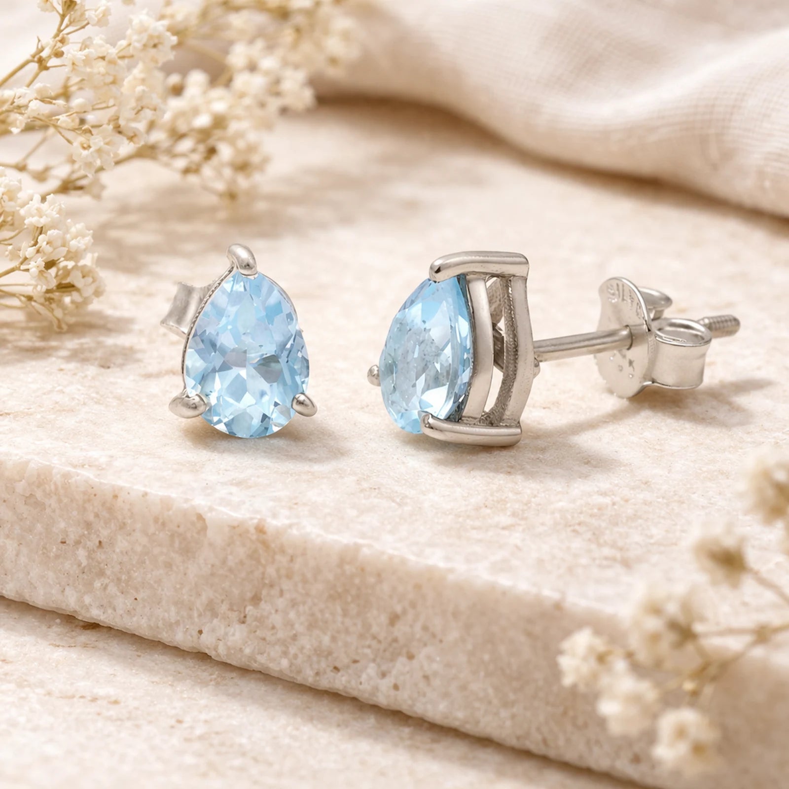 Sterling Silver Pear Shaped stud earrings with faceted blue topaz gemstones on a light surface.
