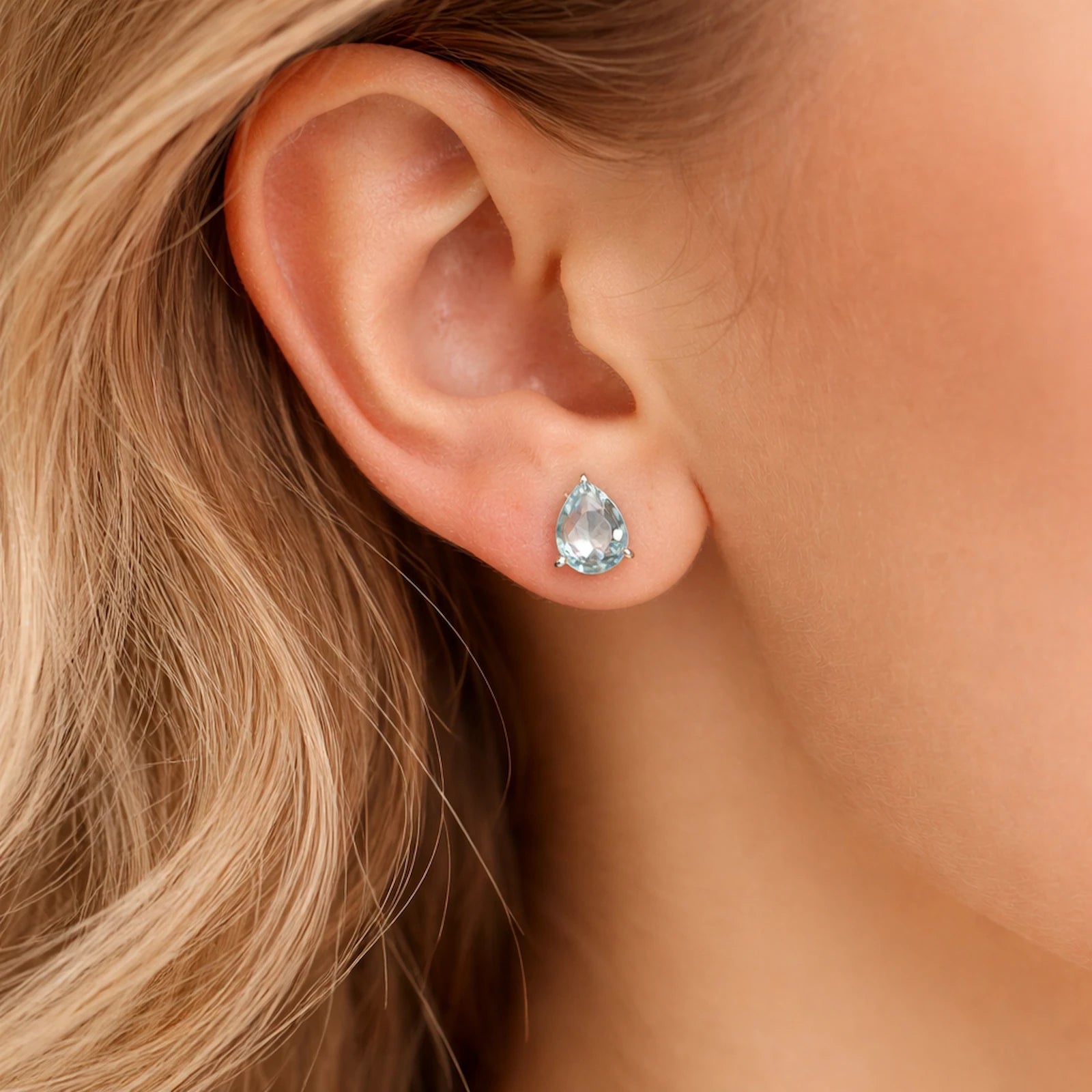 Sterling Silver Pear Shaped stud earrings with faceted blue topaz gemstones being worn.