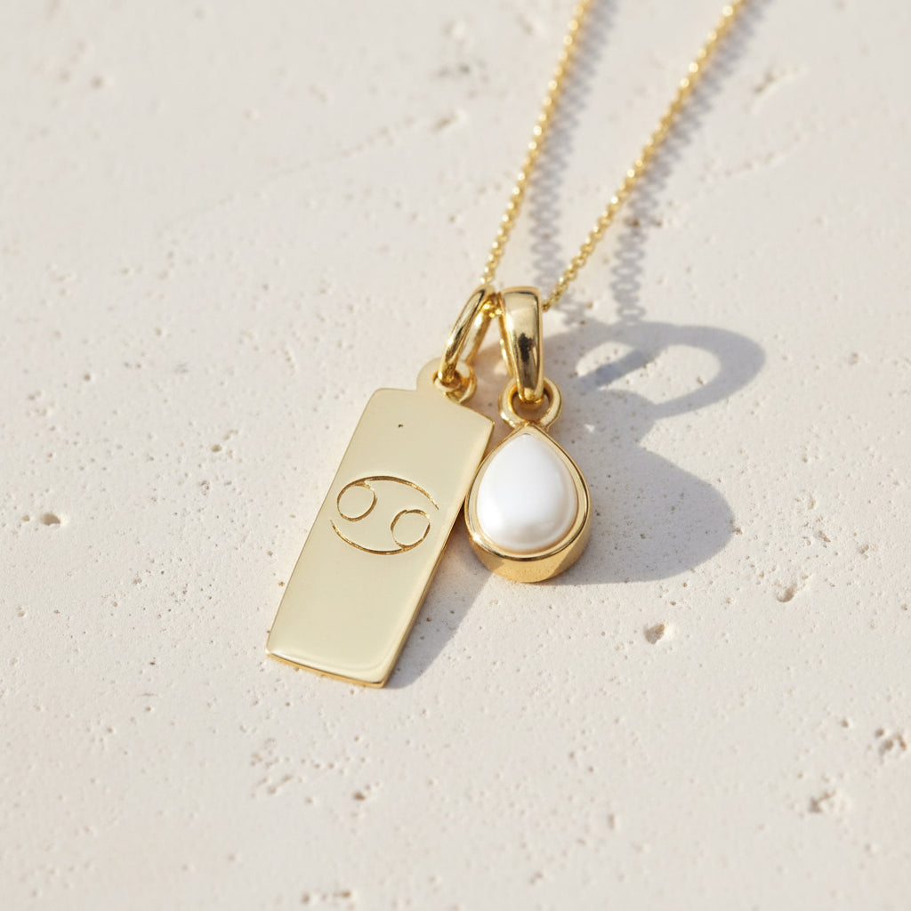 Gold necklace with cancer zodiac symbol pendant and teardrop-shaped pearl gemstone on a natural background