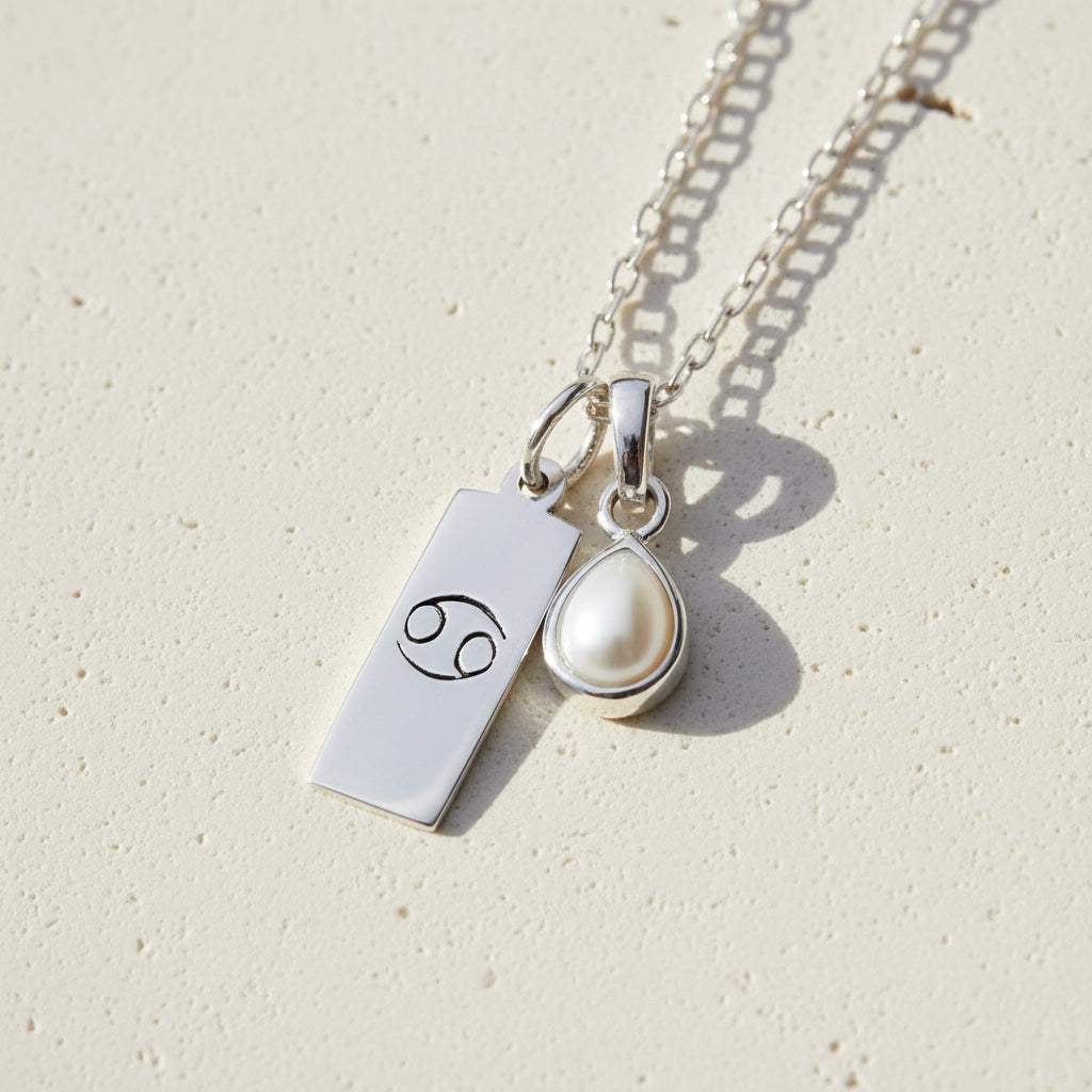Silver necklace with Cancer zodiac symbol pendant and tear drop pearl pendant on a textured background