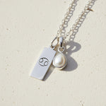Silver necklace with Cancer zodiac symbol pendant and tear drop pearl pendant on a textured background