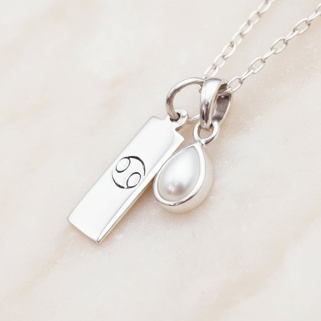 sterling silver necklace with a cancer zodiac pendant and pear shaped natural pearl pendant on a textured gold and white background