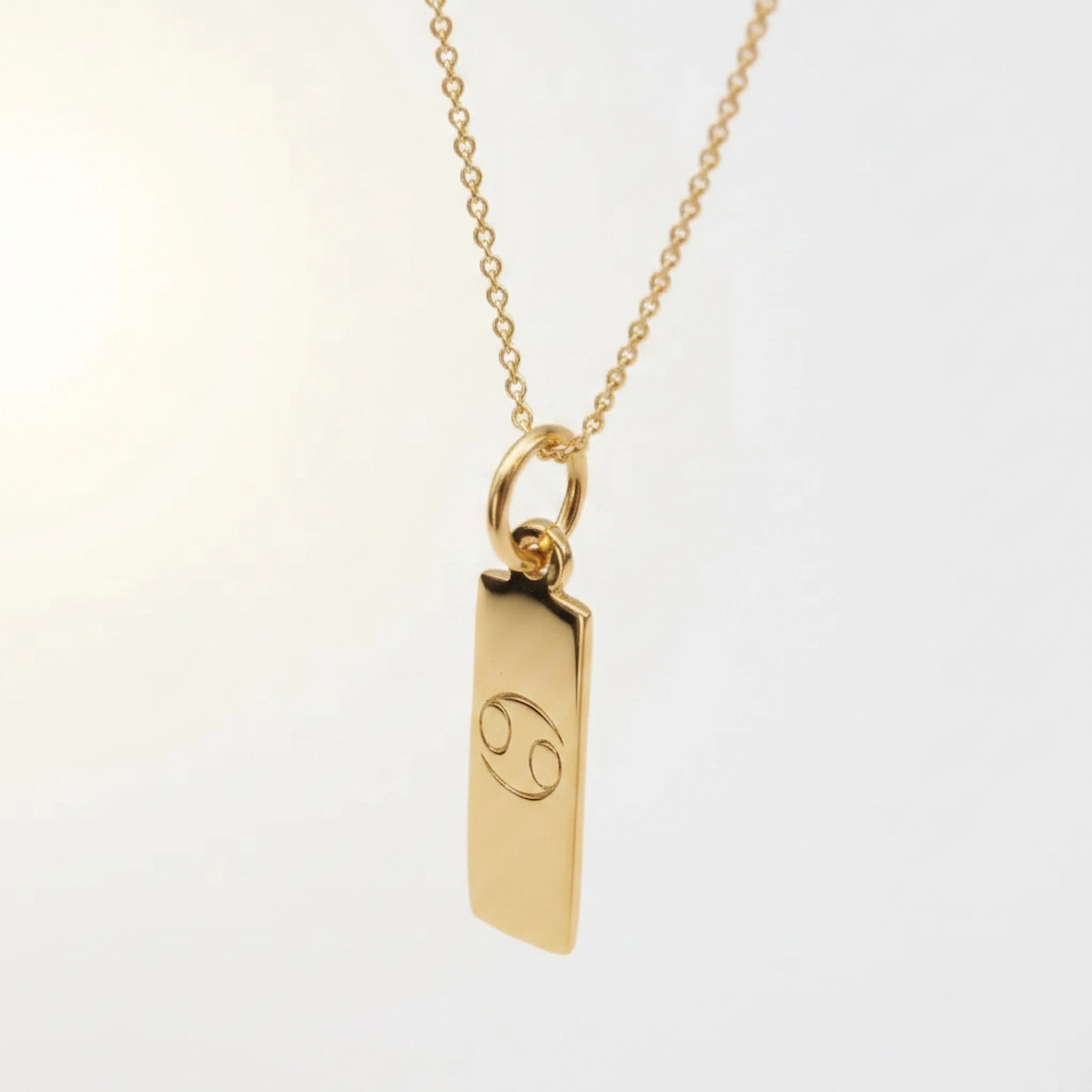 Gold pendant with cancer zodiac symbol on a light background