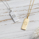 Two necklaces with rectangular pendants featuring cancer zodiac symbols on a wooden surface.