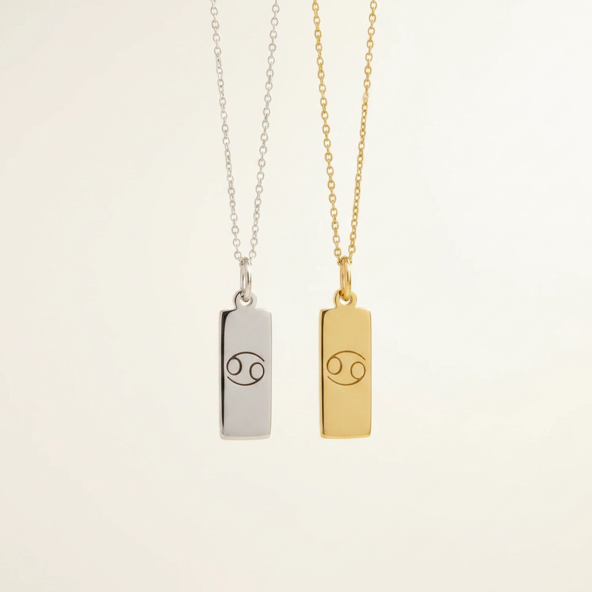 Silver and gold Cancer necklaces with engraved zodiac bar pendant necklaces with cable chains on a warm beige background