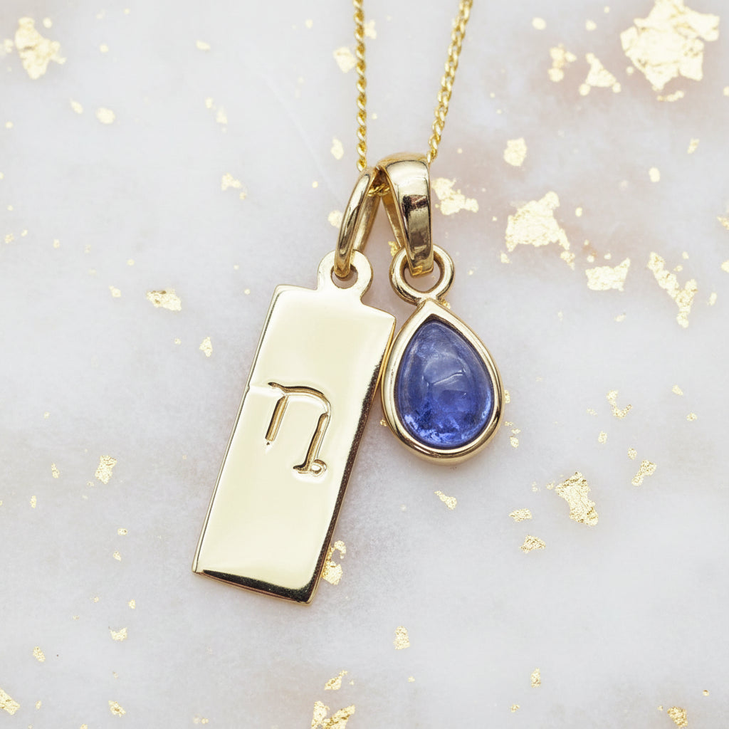 Gold capricorn zodiac pendant necklace with a blue teardrop tanzanite pendant on a gold and blue textured background.