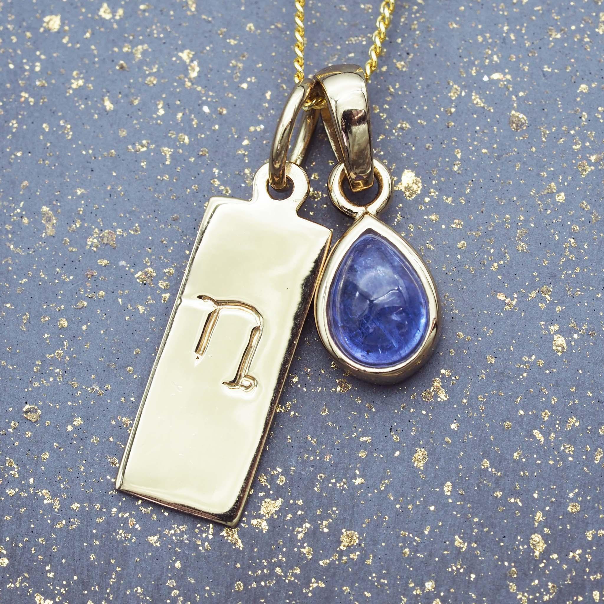 Gold capricorn zodiac pendant necklace with a blue teardrop tanzanite pendant on a gold and blue textured background.