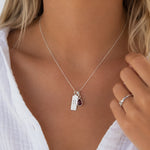 Sterling Silver necklace with a teardrop january birthstone natural garnet pendant and rectangle pendant with capricorn line glyph symbol on a person wearing a white shirt.