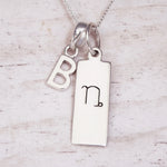 sterling silver necklace with a 'B' initial pendant and a capricorn zodiac pendant on a light wood background