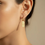 Gold huggie hoop earring with a celestial charm worn by a person with a neutral background