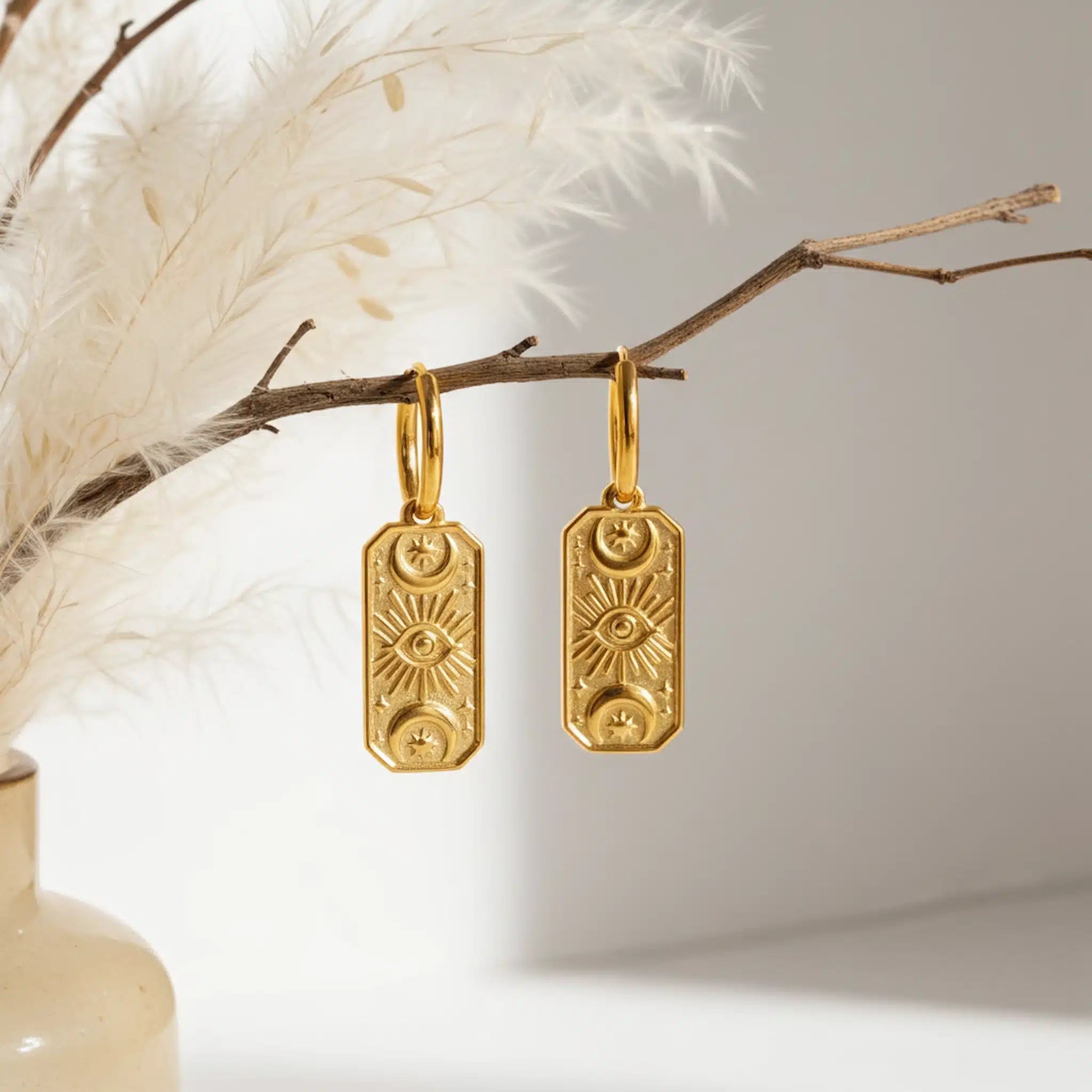 Gold hoop earrings with celestial charms hanging from a branch with a neutral background