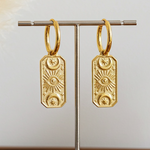 Gold hoop earrings on a stand with decorative elements on a wooden surface.