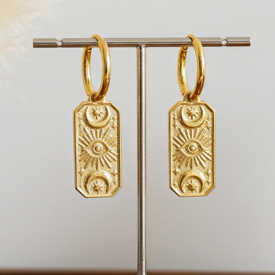 Gold hoop earrings on a stand with decorative elements on a wooden surface.