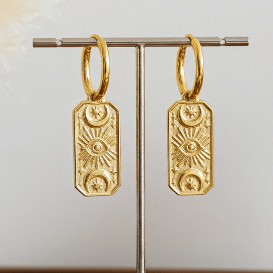 Gold hoop earrings on a stand with decorative elements on a wooden surface.