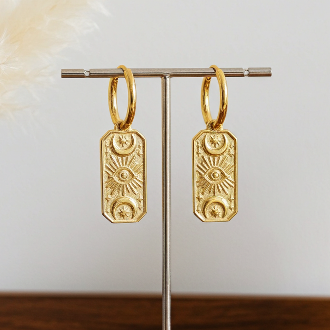 Celestial Gold hoop earrings on a stand with decorative elements on a wooden surface.