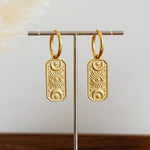 Gold hoop earrings with celestial charms on a stand against a neutral background
