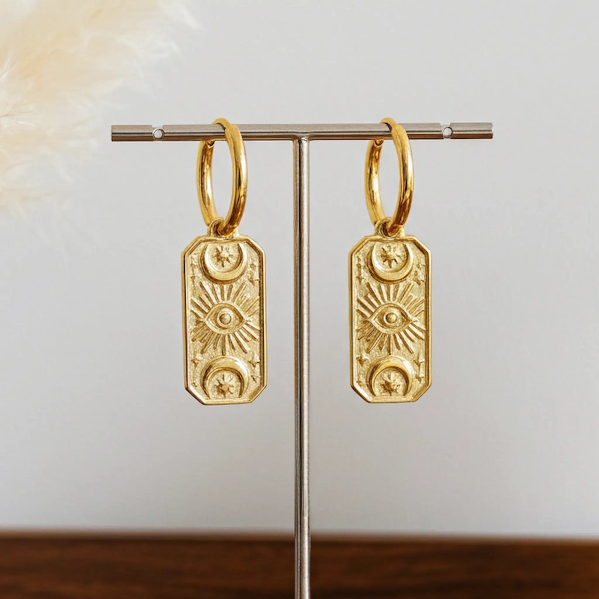 Gold hoop earrings with celestial charms on a stand against a neutral background