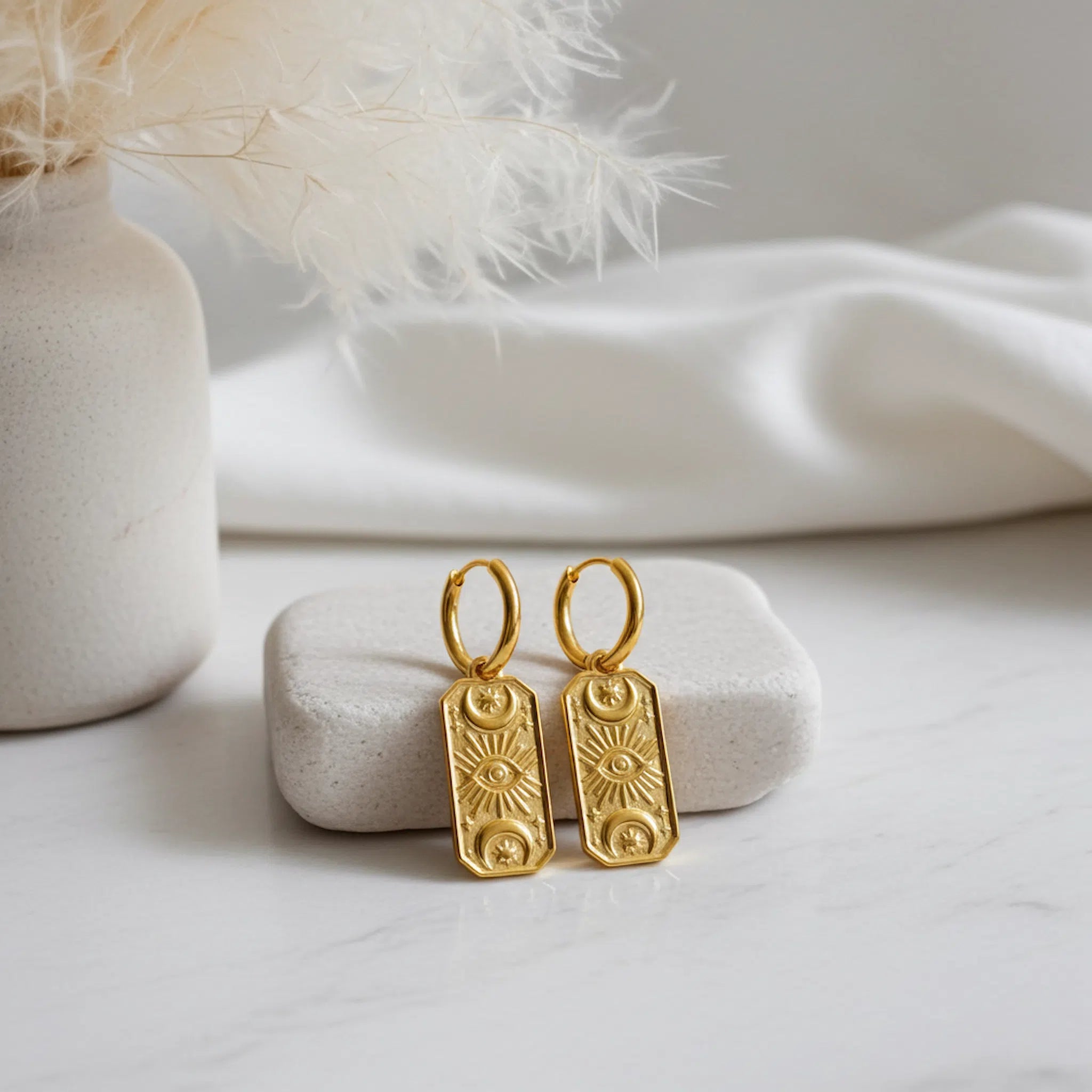 Gold huggie hoop earrings with celestial charms on a white stone with a soft background