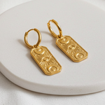 Gold earrings on a white ceramic plate with a soft white background