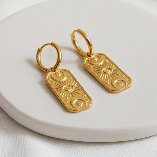 Gold earrings on a white ceramic plate with a soft white background