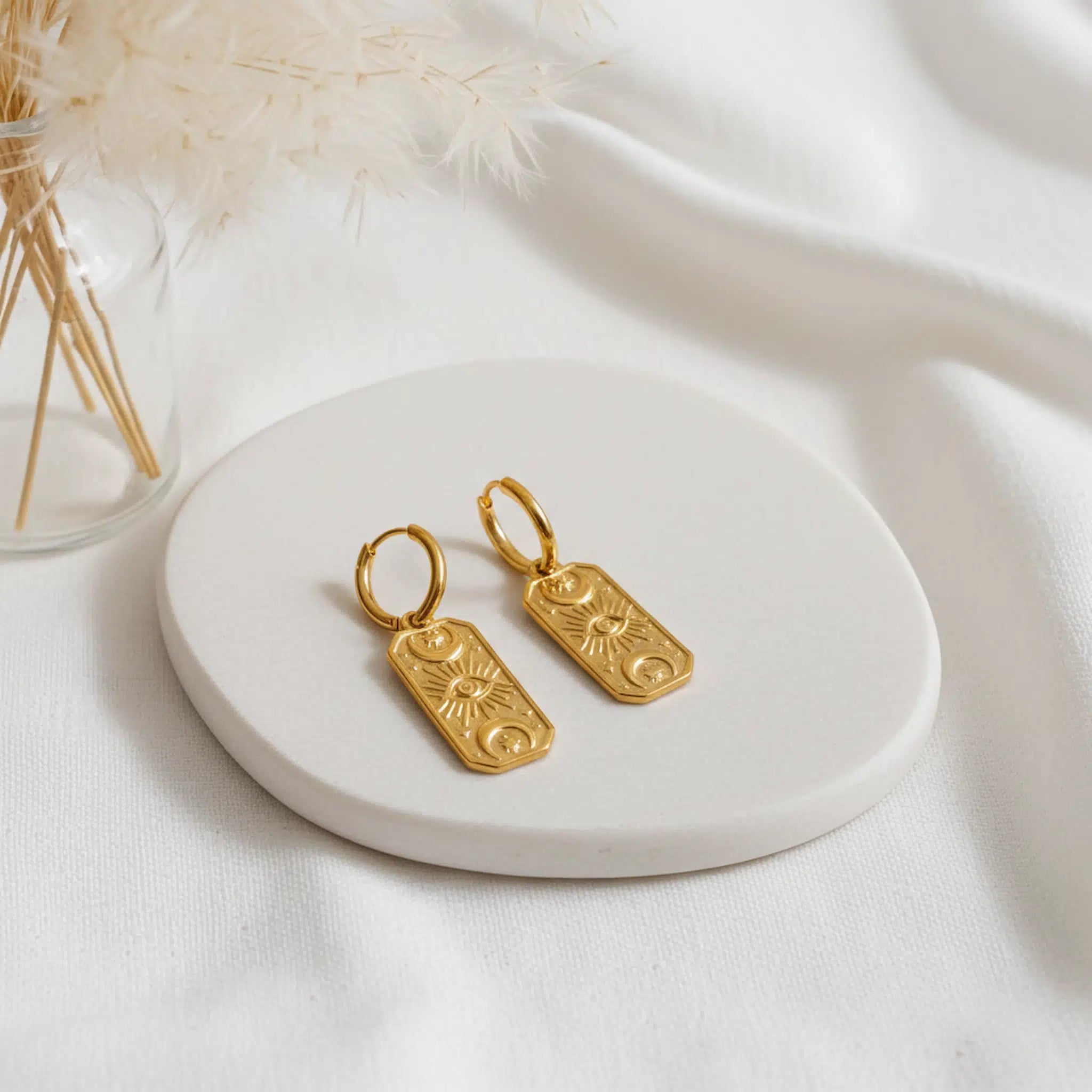 Gold huggie hoop earrings with celestial charms on a white stone surface with a soft background
