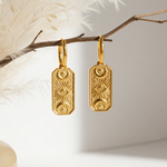 Gold earrings hanging from a branch with a neutral background