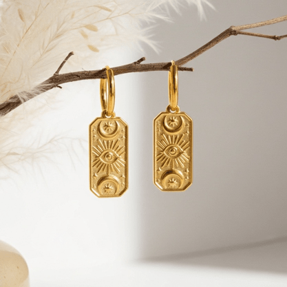 Gold earrings hanging from a branch with a neutral background