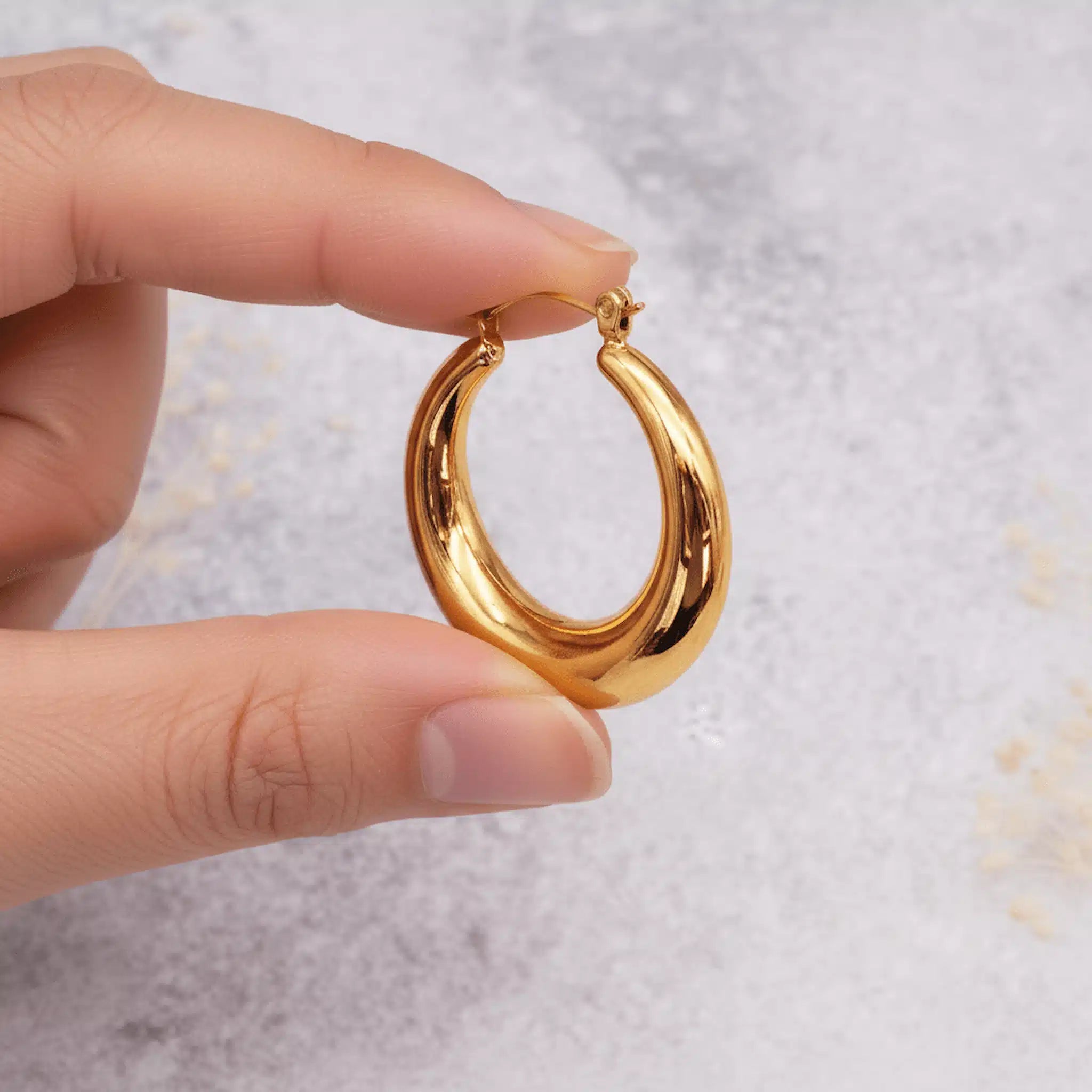 fingers holding a stainless steel chunky gold waterproof hoop earring