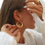 Close-up of a person wearing a white woollen jumper and stainless steel chunky gold waterproof hoop earrings 