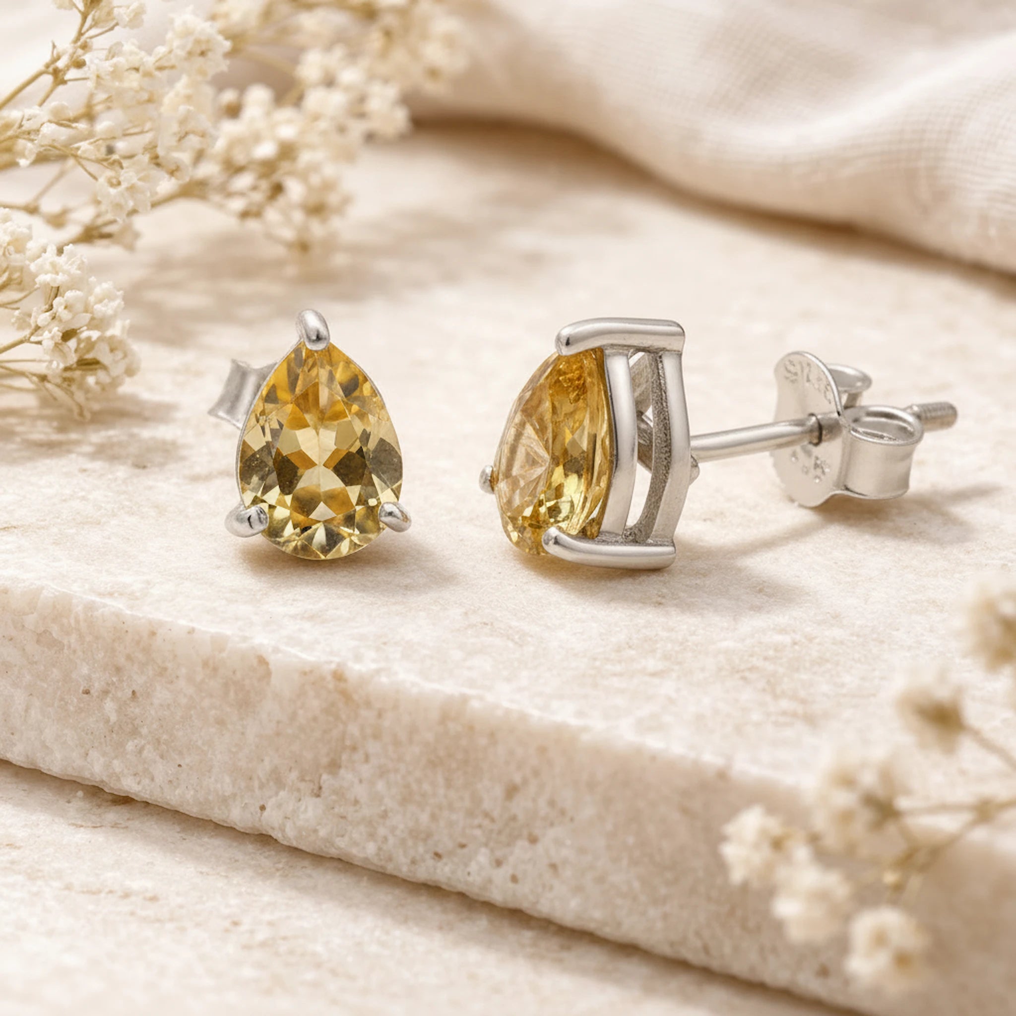 Pair of yellow citrine gemstone earrings on a beige surface with small white flowers.