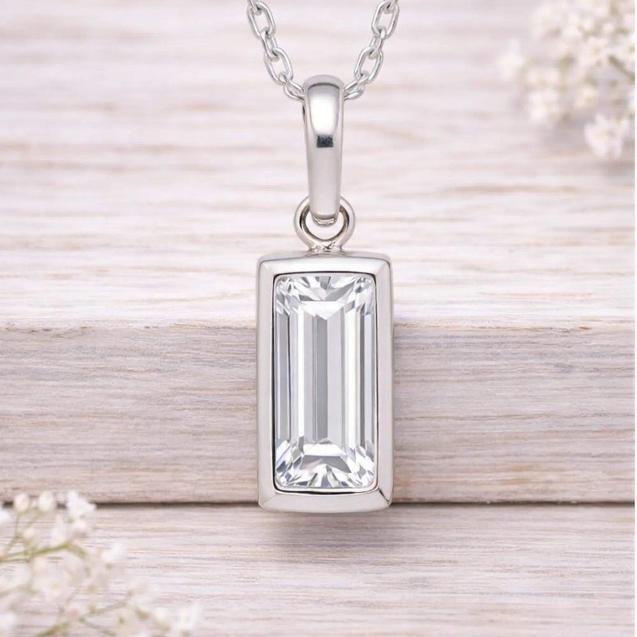 Silver waterproof necklace pendant with rectangular gemstone on a light wooden background