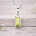 Silver waterproof necklace pendant with a green gemstone on a wooden surface