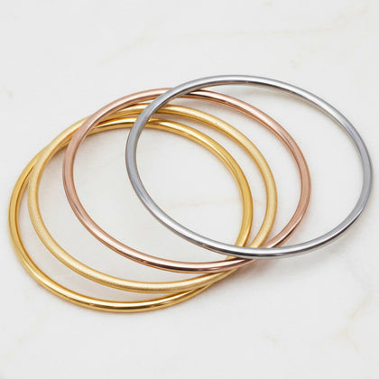 Four metallic bangles in gold, rose gold, and silver on a light background