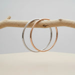 Two bangles, one silver and one rose gold, on a branch with a neutral background.