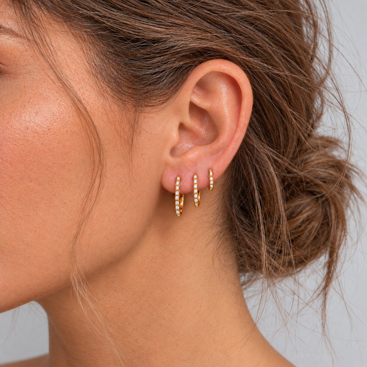 Model with tousled hair wearing three slim gold CZ pavé huggie hoops in 6 mm, 8 mm and 10 mm sizes