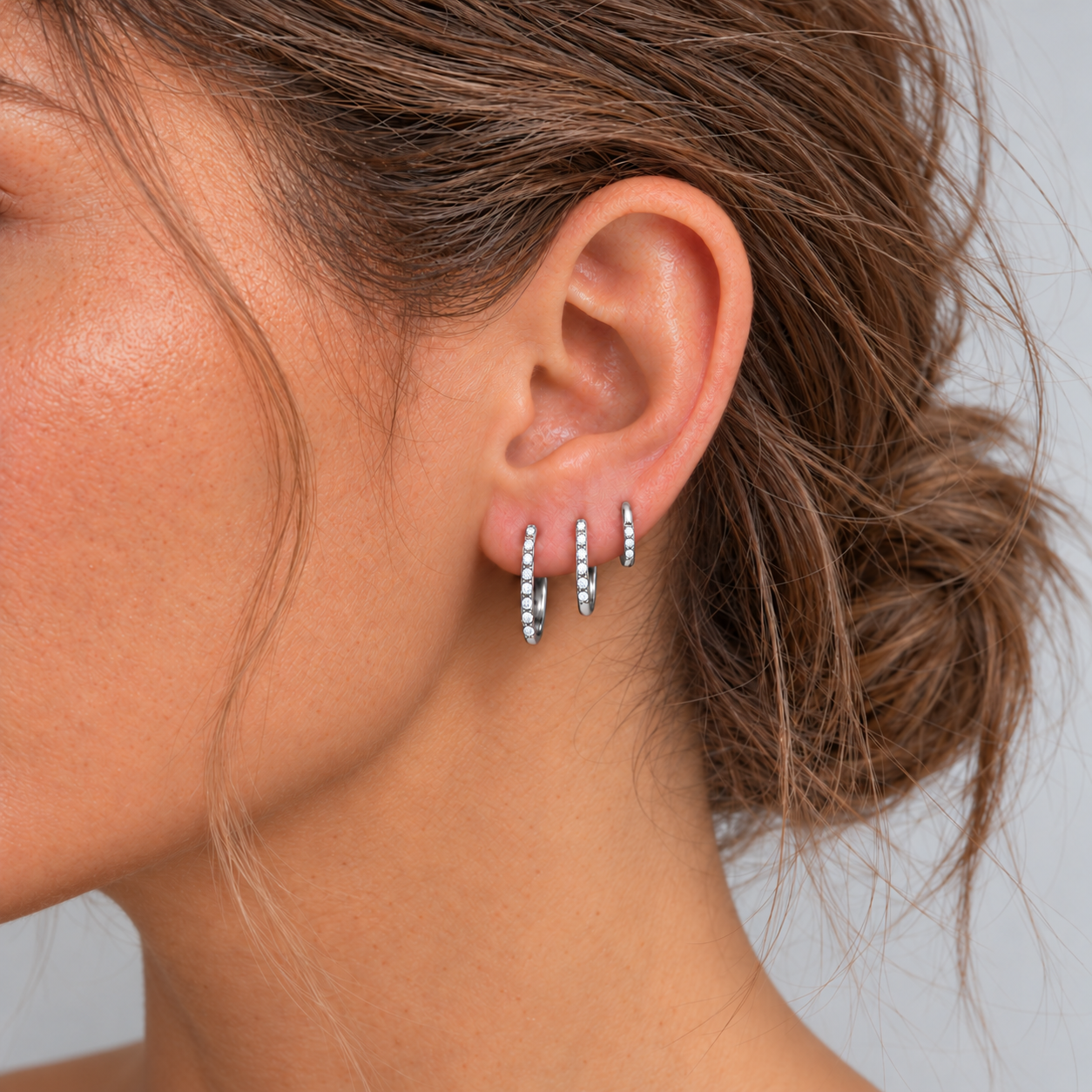 Model wearing three slim silver CZ pavé huggie hoop earrings in 6 mm, 8 mm and 10 mm sizes