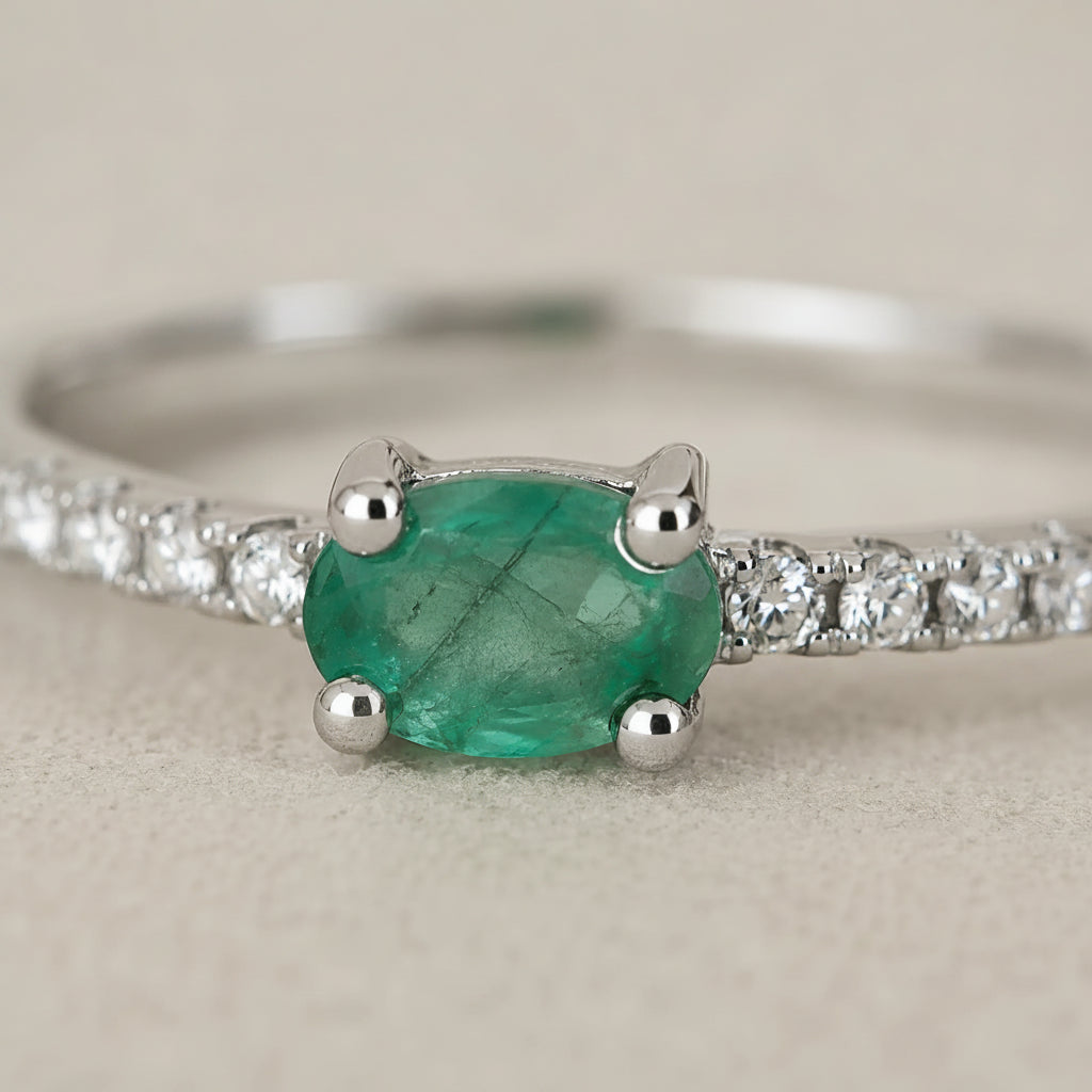 close up of a Classic Sterling Silver Pave Stacking ring with a oval faceted claw set emerald gemstone on a beige background.