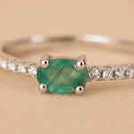 close up of a Classic Sterling Silver Pave Stacking ring with a oval faceted claw set emerald gemstone on a beige background.