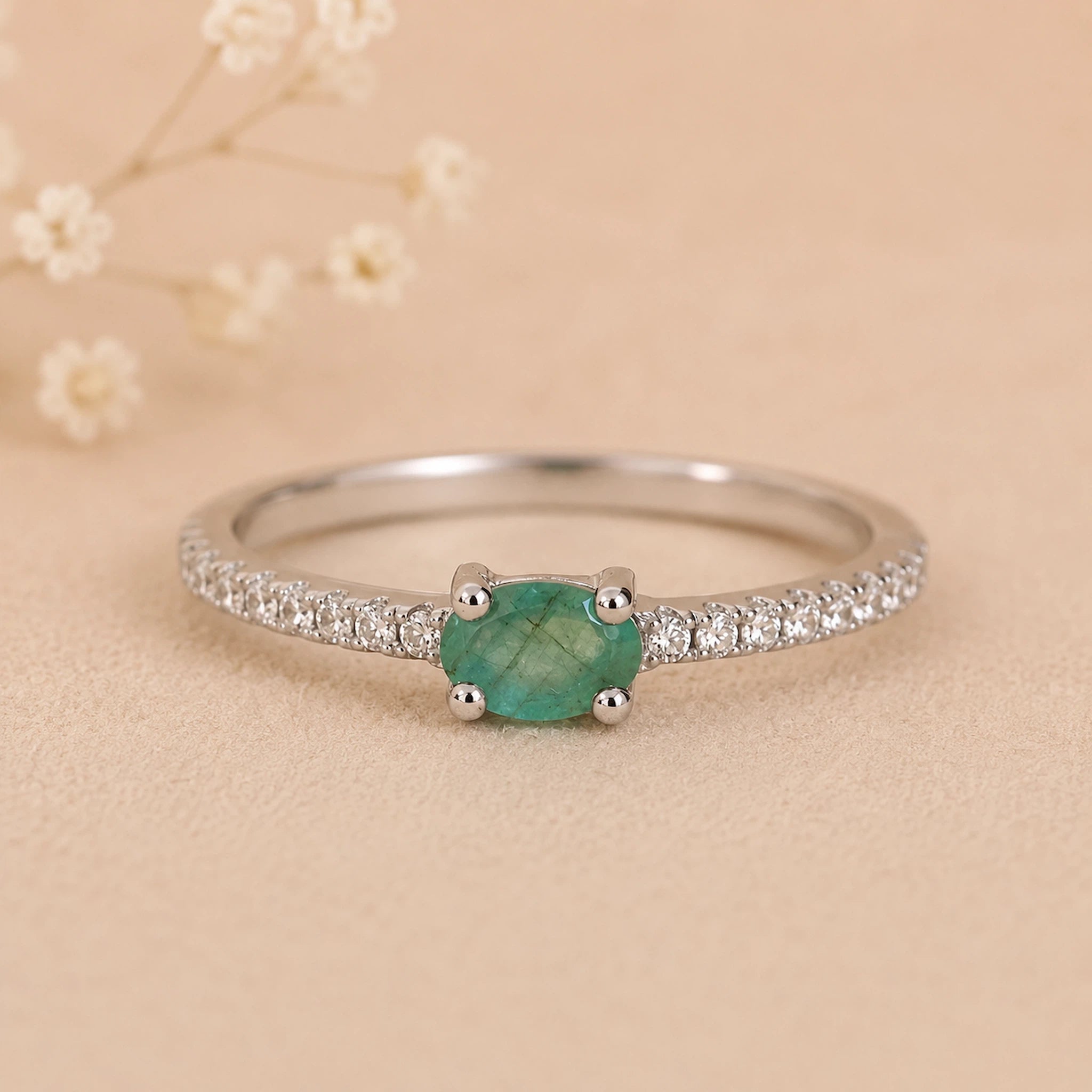 Classic Sterling Silver Pave Stacking ring with a oval faceted claw set emerald gemstone on a beige background.