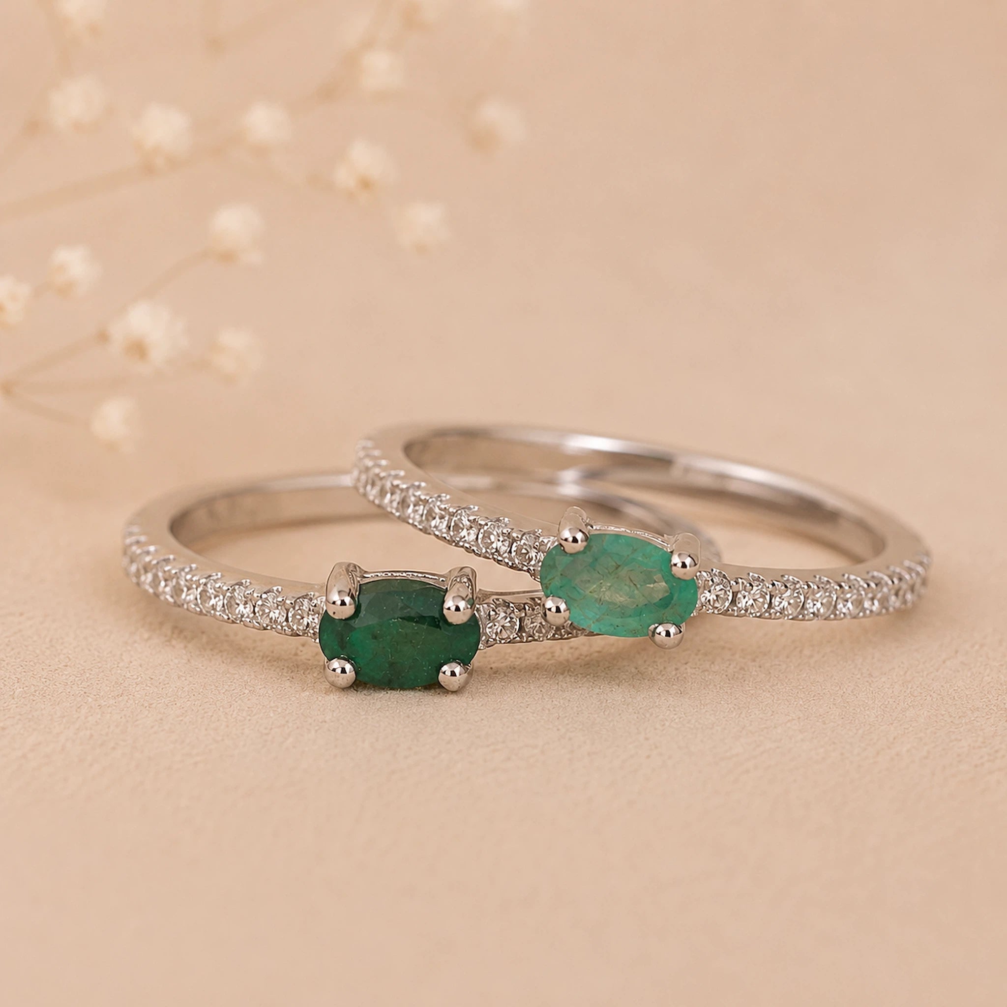 Two Classic Sterling Silver Pave Stacking rings with a oval faceted claw set emerald gemstones on a beige background.