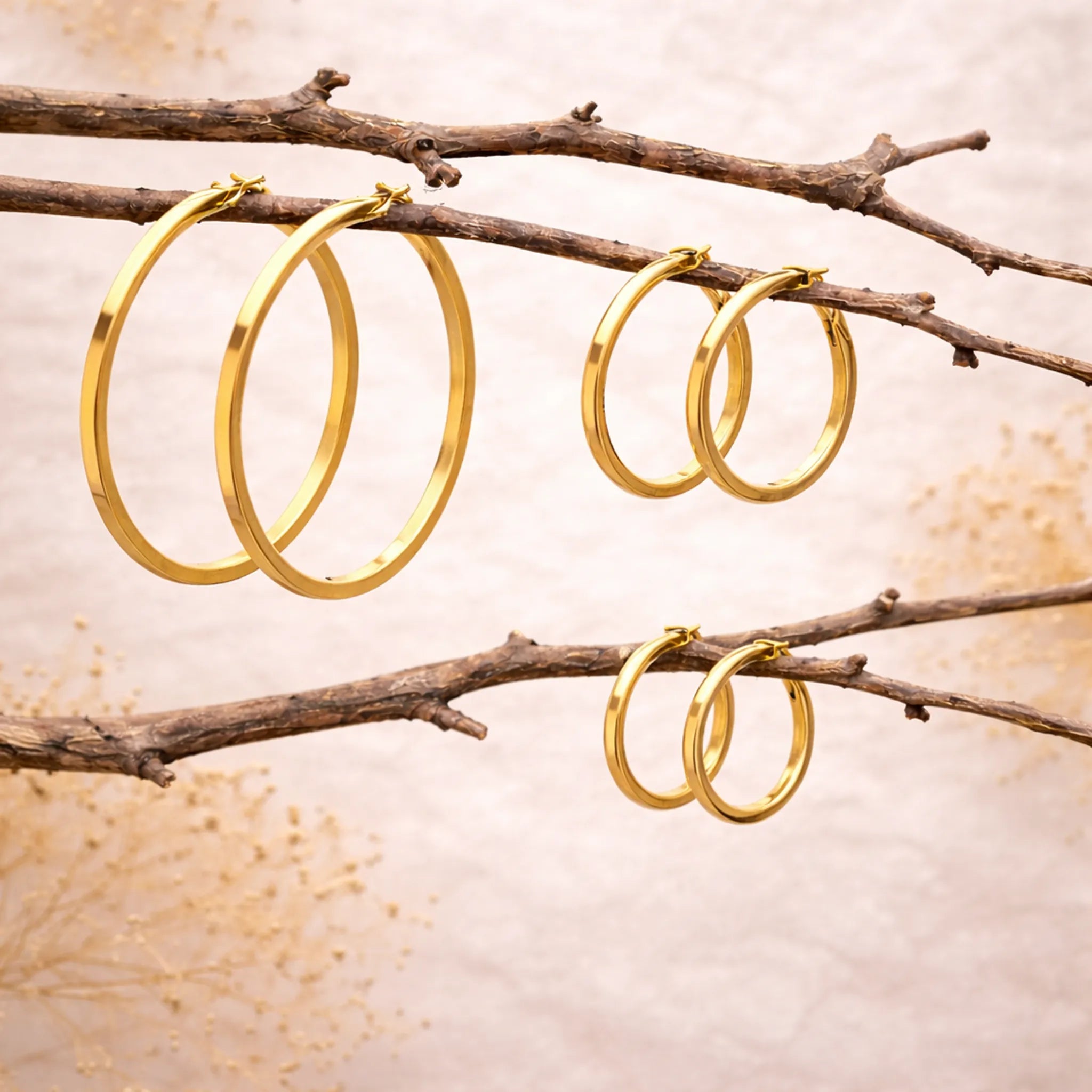 three pairs of Gold Hoop Earrings in waterproof stainless steel hanging from branches
