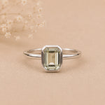 Sterling Silver ring with a emerald-cut, bezel set green amethyst gemstone on a beige background