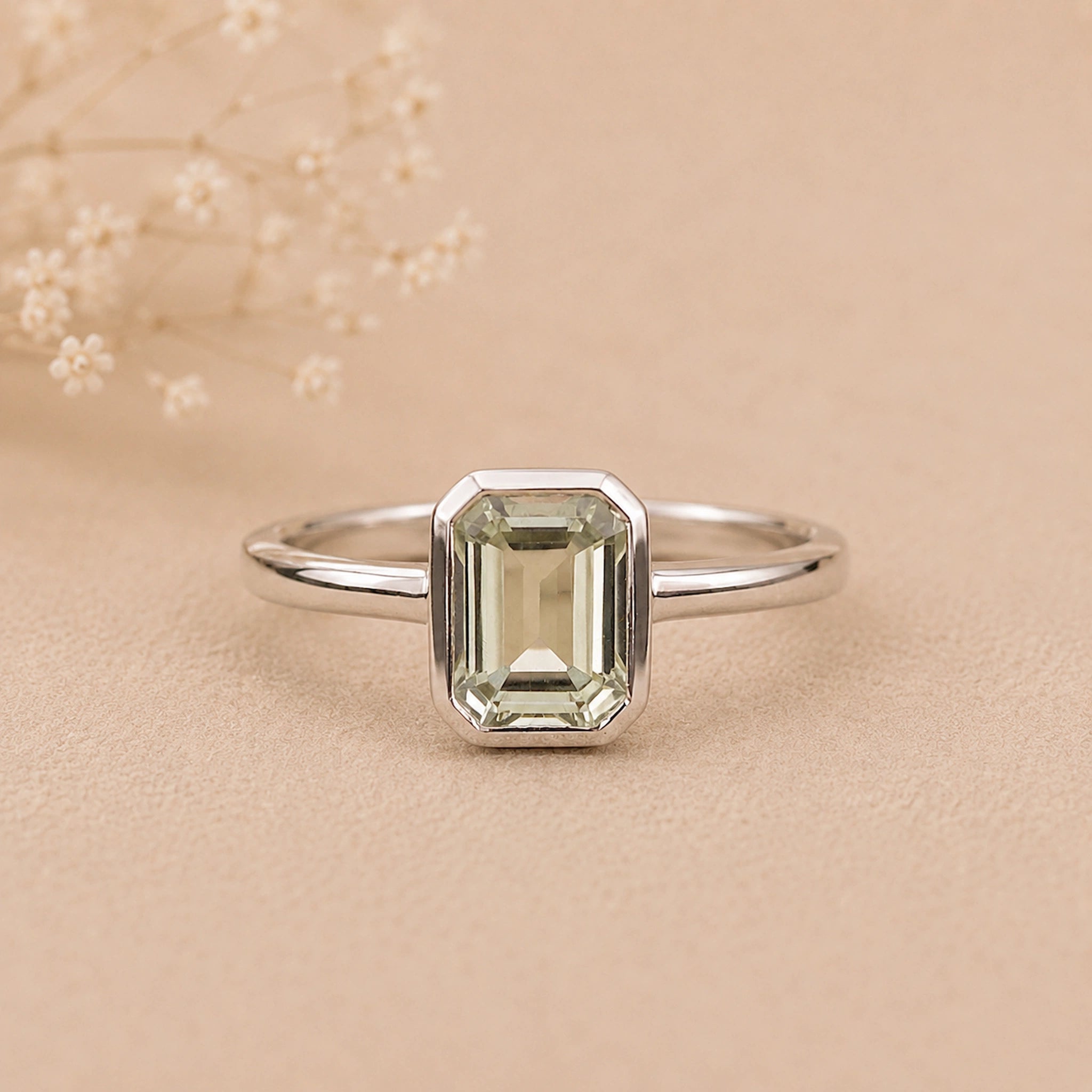Sterling Silver ring with a emerald-cut, bezel set green amethyst gemstone on a beige background